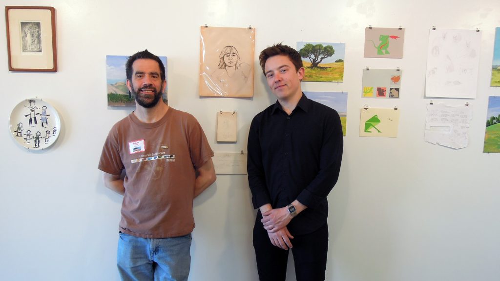 A photo of Sam and Tom in front of a gallery wall showing Nina's artwork.